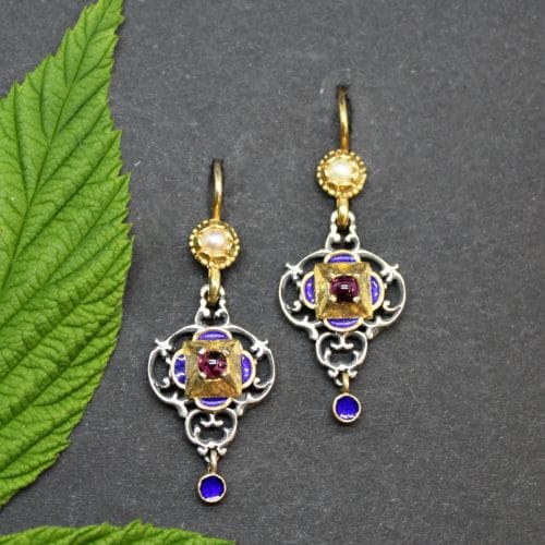 Traditionelle Trachtenschmuck Ohrringe in Silber und vergoldeten und emaillierten Details in Blau. Der Ohrschmuck ist mit Granat gefasst